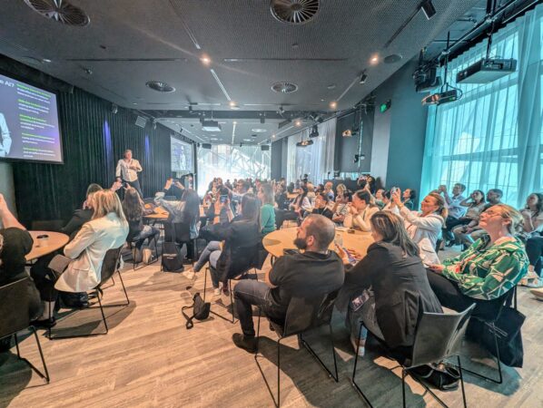 a man on stage talking to an audience with a slideshow on a screen. they are all paying close attention. 